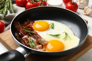 Tasty bacon, eggs and rosemary in frying pan on light table, closeup