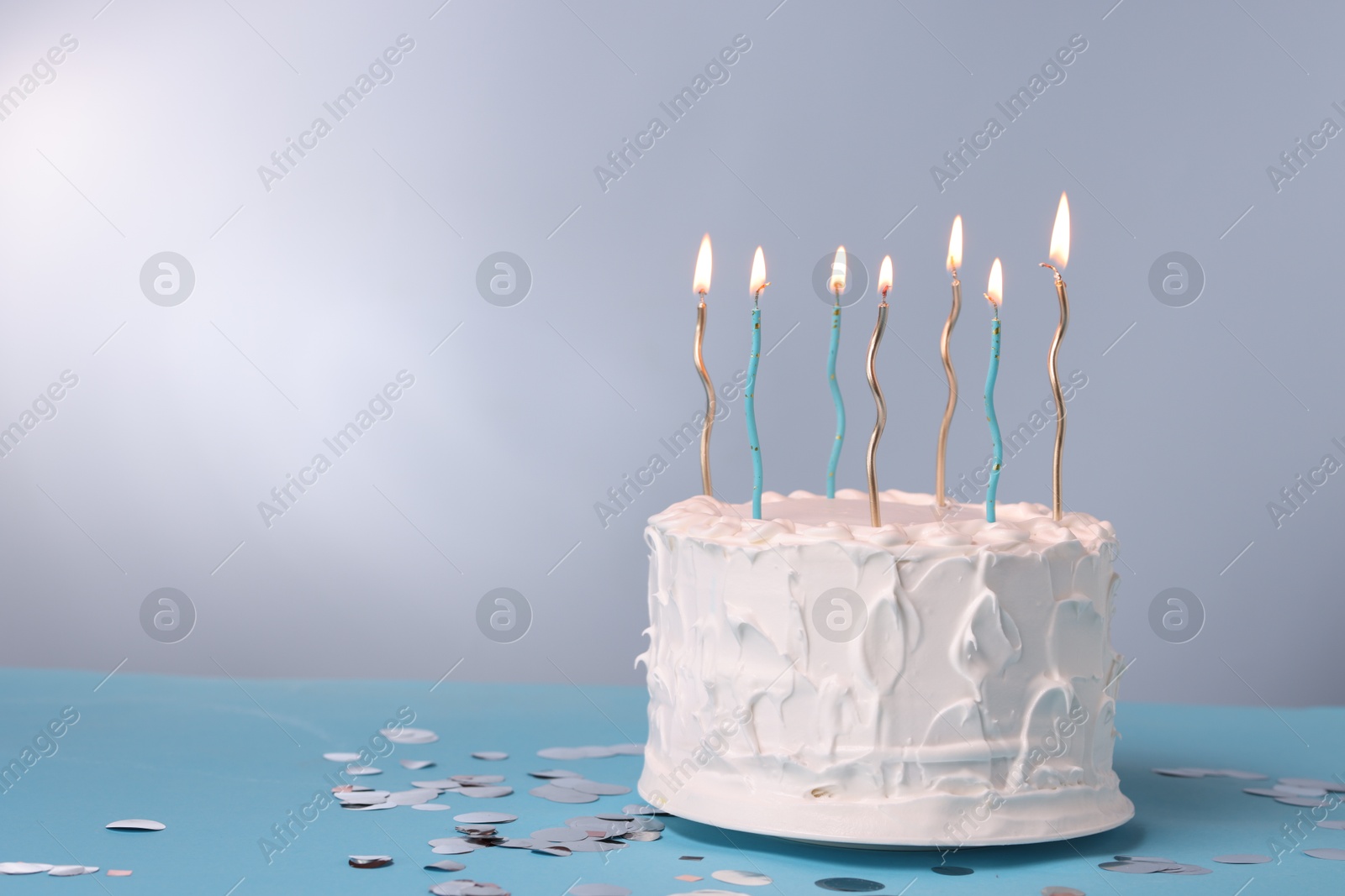 Photo of Tasty Birthday cake with burning candles and confetti on light blue table against gray background, space for text