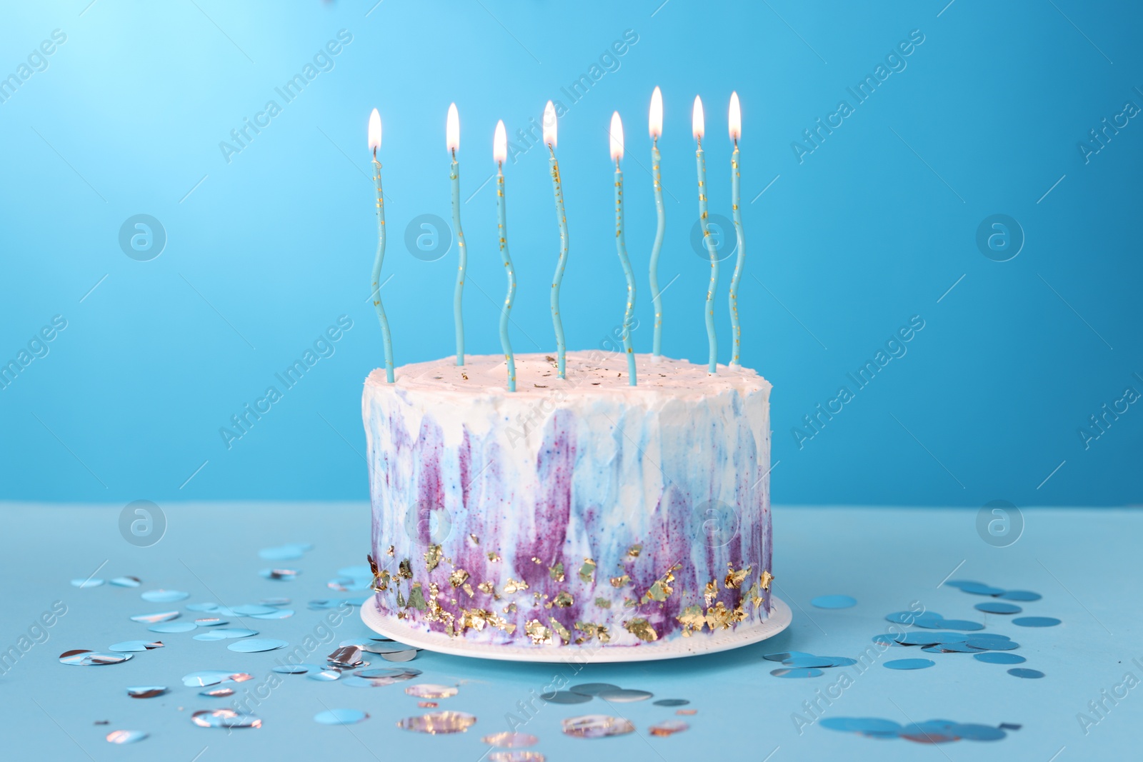 Photo of Tasty Birthday cake with burning candles and confetti on light blue table