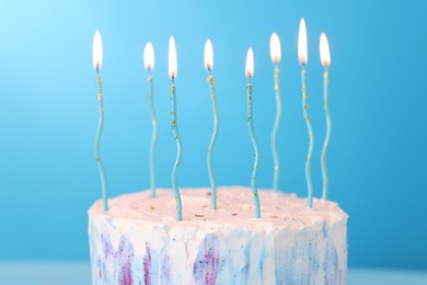 Photo of Tasty Birthday cake with burning candles on light blue background, closeup