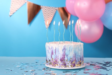 Tasty Birthday cake with burning candles and confetti on light blue table