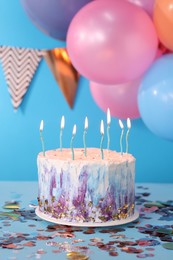 Photo of Tasty Birthday cake with burning candles and party decor on light blue background