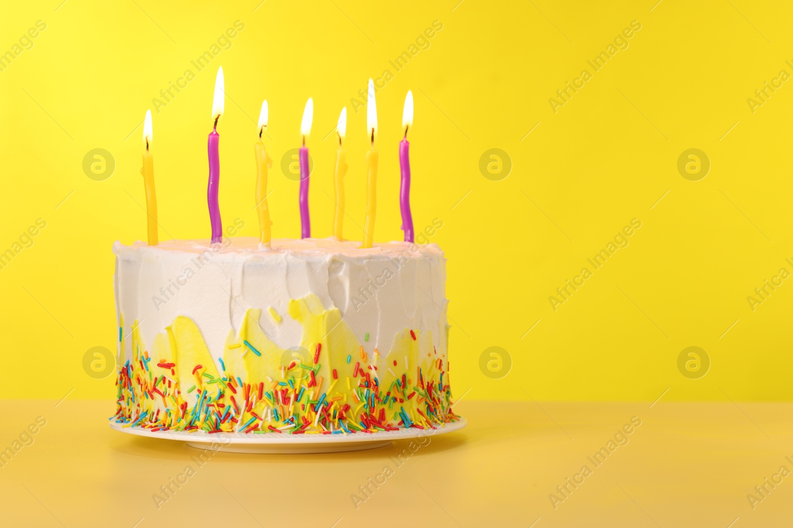 Photo of Tasty Birthday cake with burning candles on yellow background, space for text