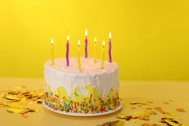 Photo of Tasty Birthday cake with burning candles and confetti on yellow table, space for text