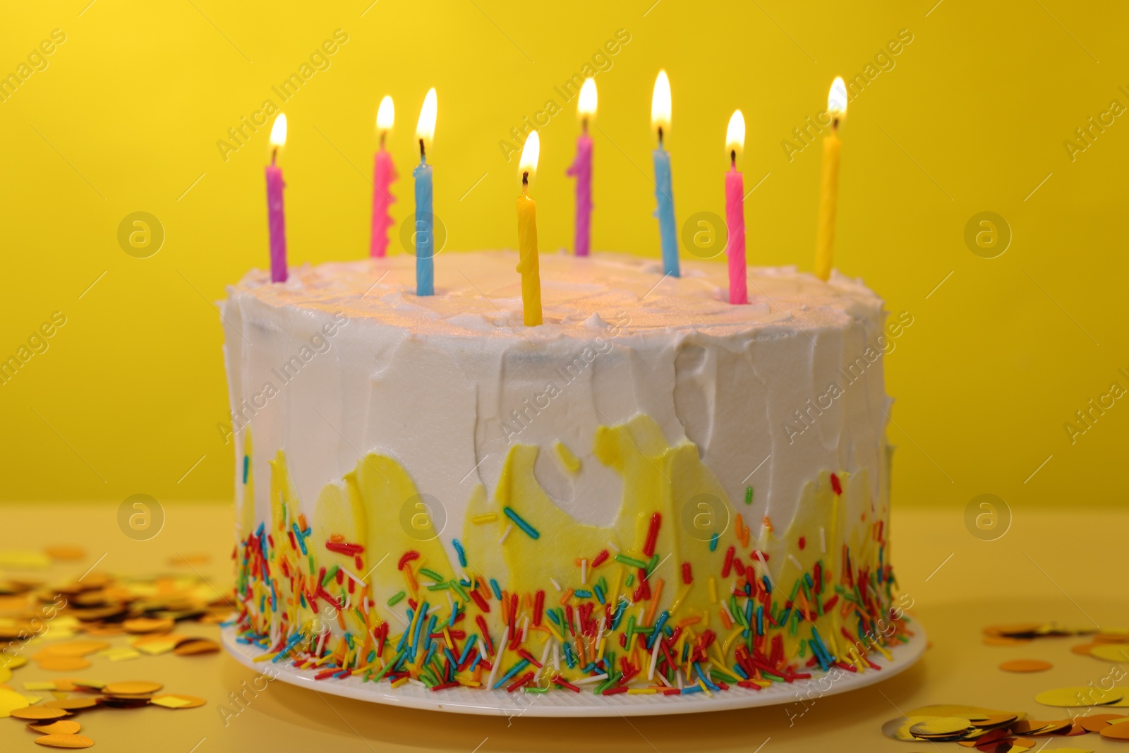 Photo of Tasty Birthday cake with burning candles and confetti on yellow table, closeup