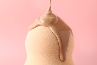 Photo of Pouring skin foundation onto makeup sponge against pink background, closeup