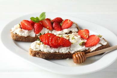 Photo of Delicious ricotta bruschettas with strawberry and pistachios served with honey on white table, closeup
