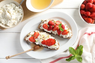 Photo of Delicious ricotta bruschettas with strawberry, mint and pistachios served with honey on white wooden table, flat lay