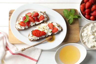 Delicious ricotta bruschettas with strawberry, mint and pistachios served with honey on white wooden table, flat lay