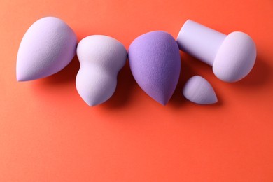 Photo of Many colorful makeup sponges on orange background, flat lay. Space for text