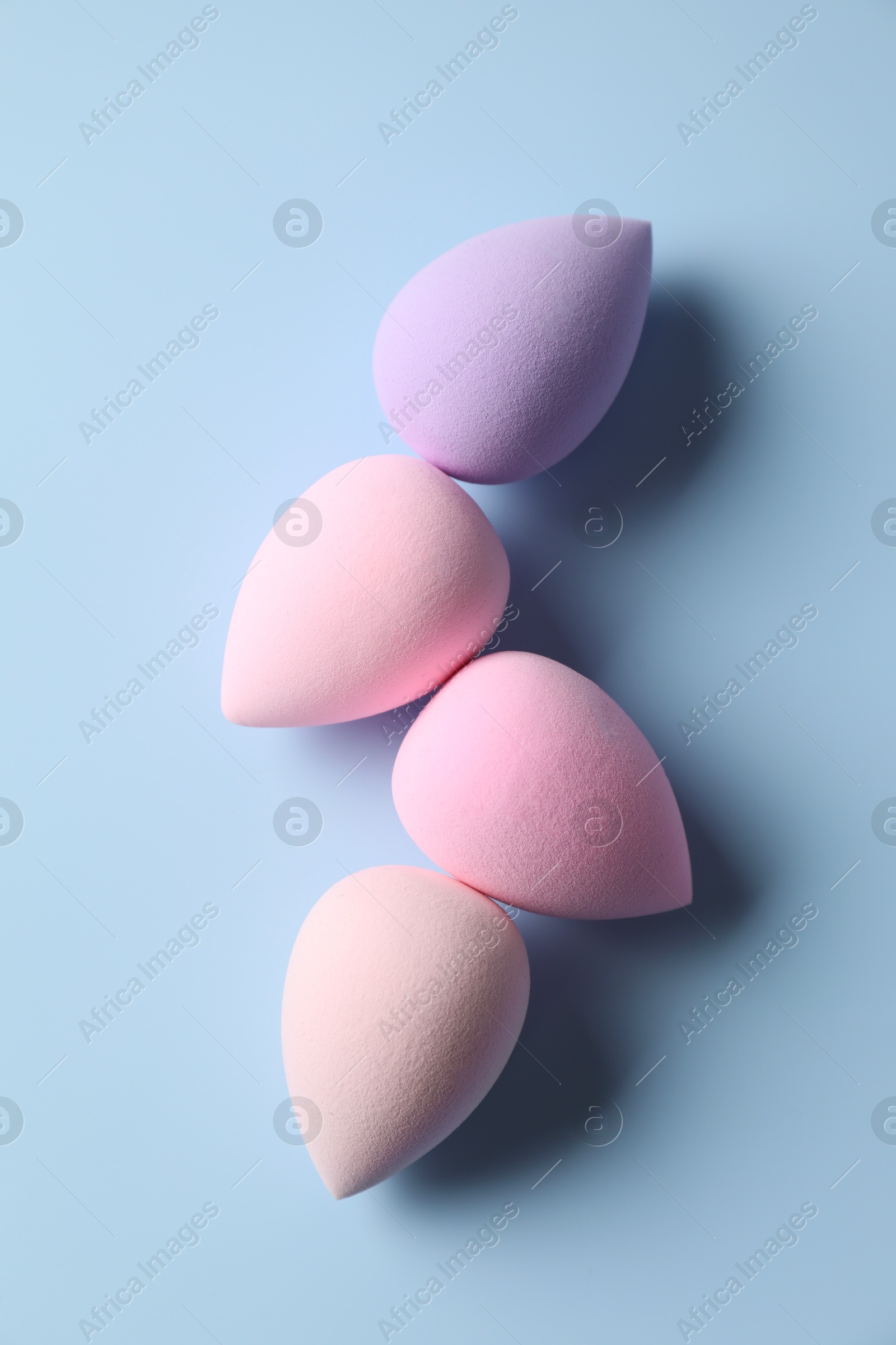 Photo of Many colorful makeup sponges on light blue background, flat lay