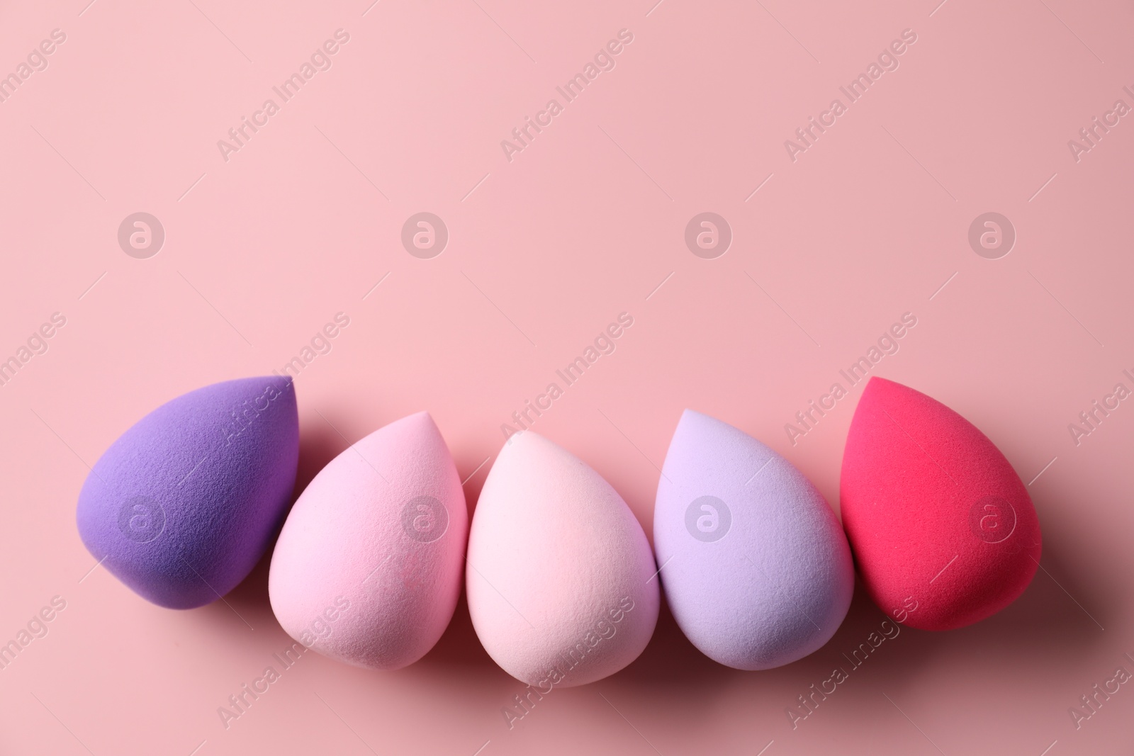 Photo of Many colorful makeup sponges on pink background, flat lay. Space for text