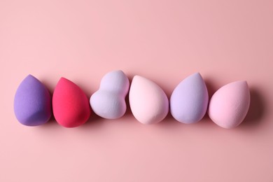 Photo of Many colorful makeup sponges on pink background, flat lay