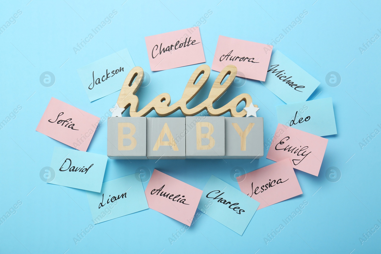 Photo of Cubes with phrase Hello Baby and paper stickers with different names on light blue background, flat lay. Choosing baby's name