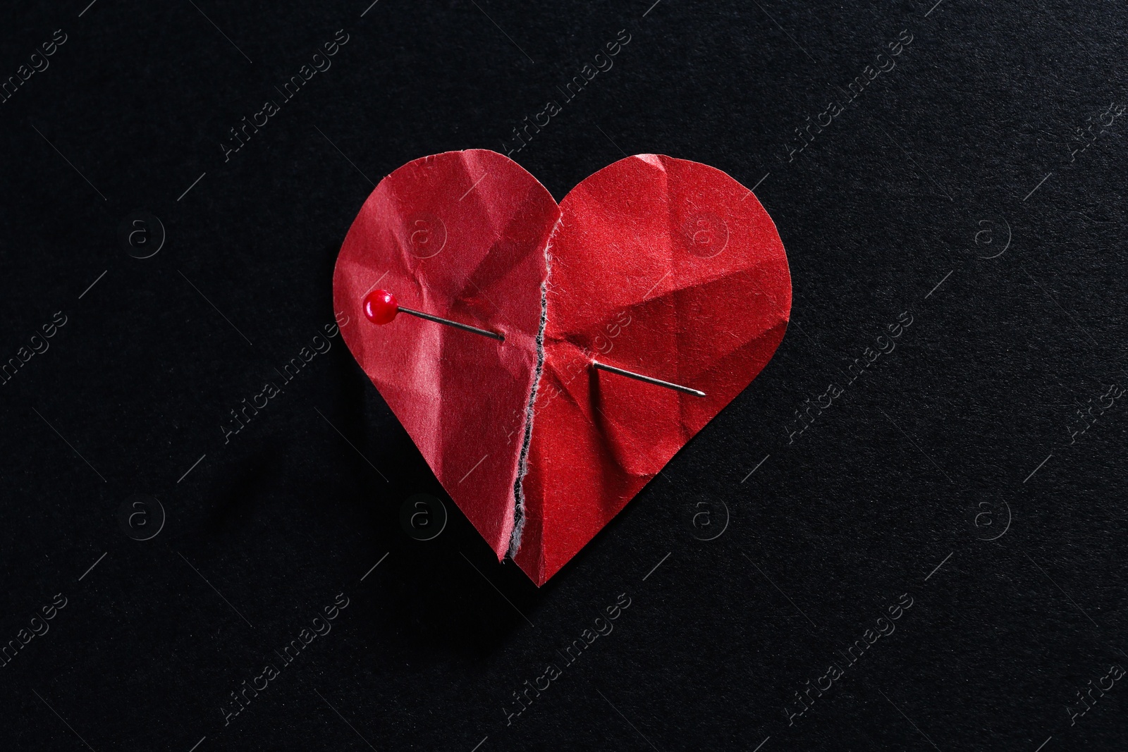 Photo of Halves of torn paper heart connected by sewing pin on black background. Relationship problem concept