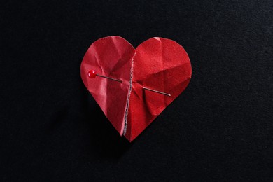 Photo of Halves of torn paper heart connected by sewing pin on black background. Relationship problem concept