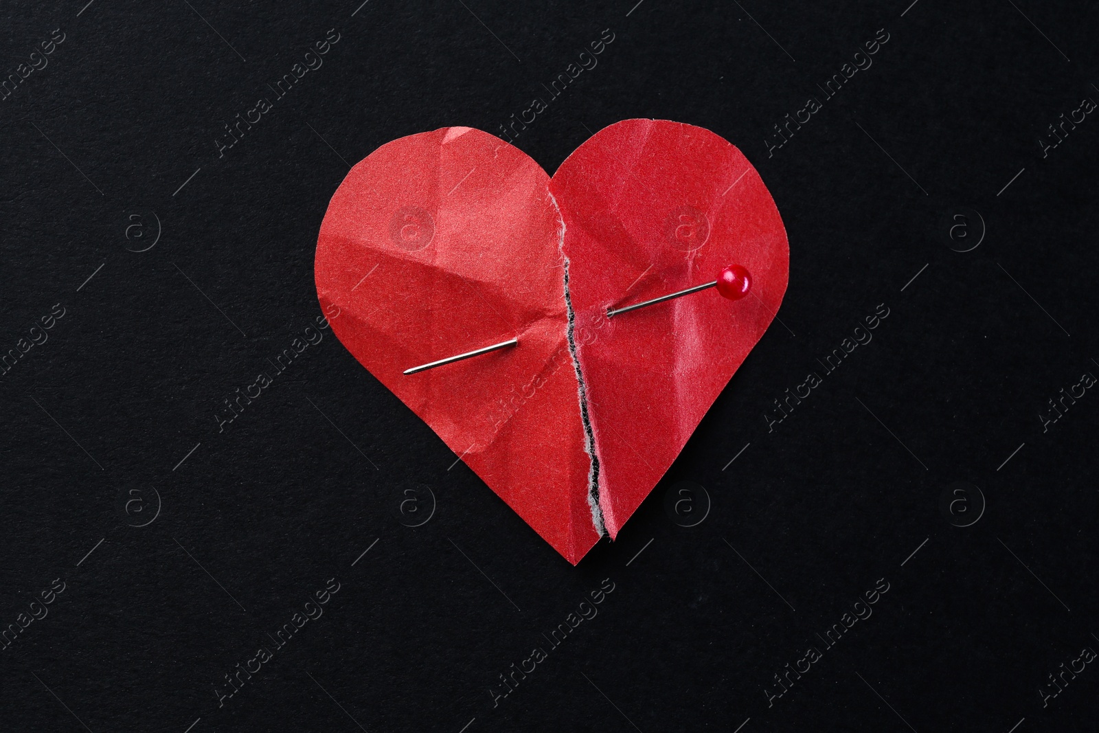 Photo of Halves of torn paper heart connected by sewing pin on black background, top view. Relationship problem concept