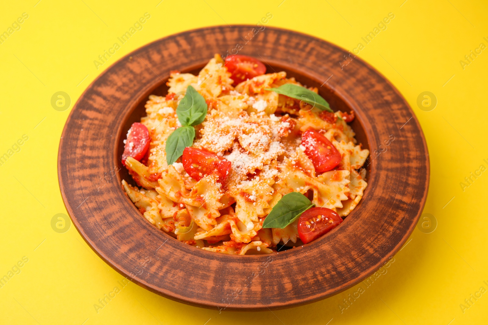 Photo of Tasty pasta with tomato, cheese and basil on yellow table