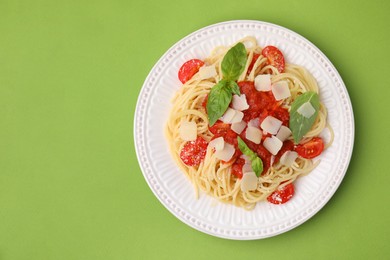 Tasty pasta with tomato sauce, cheese and basil on green table, top view. Space for text