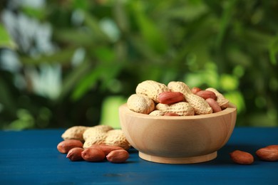 Fresh unpeeled peanuts in bowl on blue wooden table against blurred background
