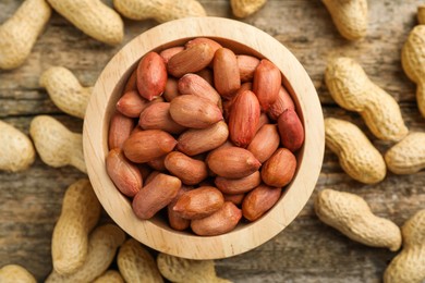 Fresh unpeeled peanuts in bowl on wooden table, top view