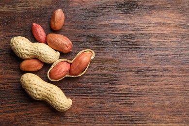 Photo of Fresh unpeeled peanuts on wooden table, top view. Space for text