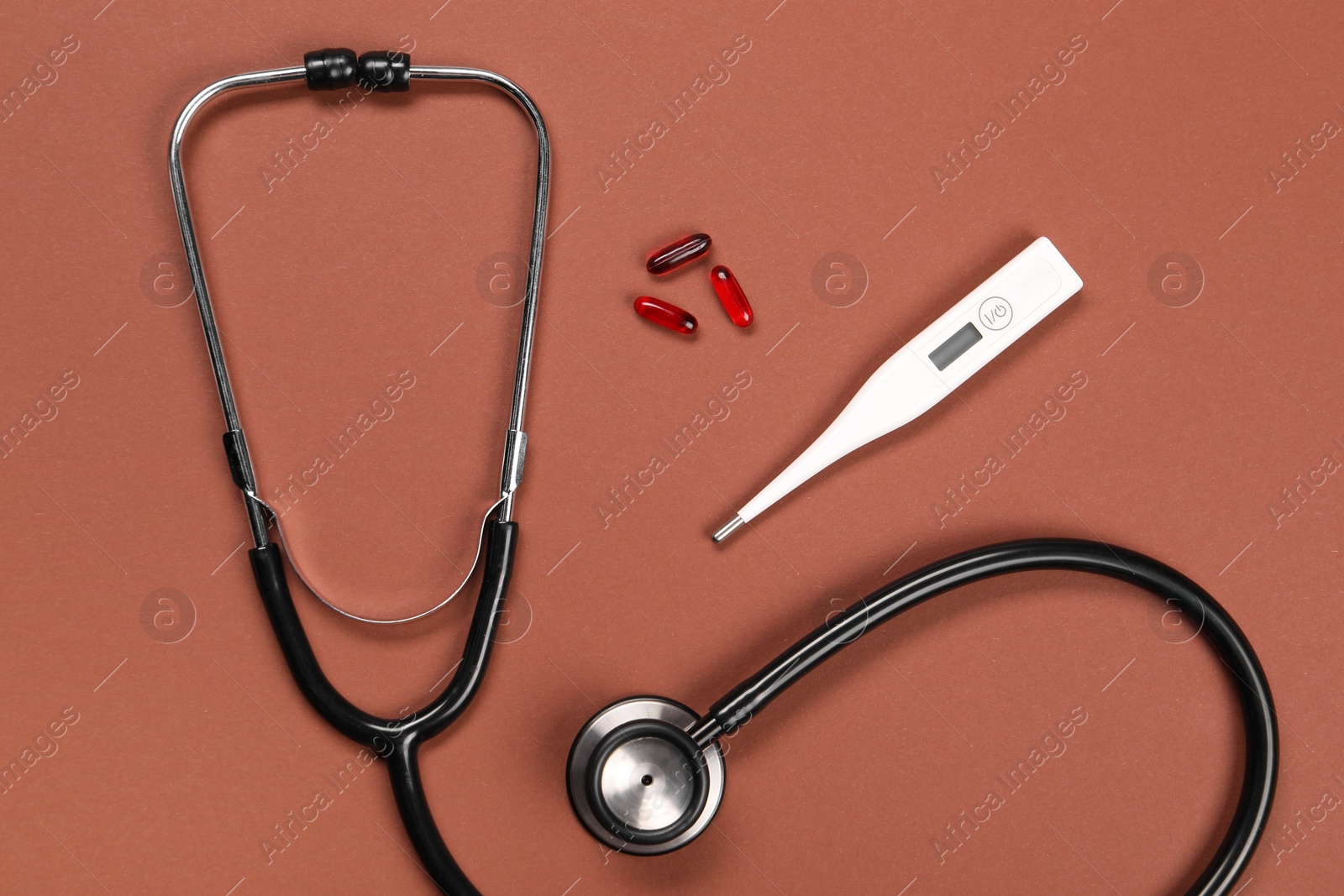 Photo of Stethoscope, thermometer and pills on brown background, flat lay. Medical treatment