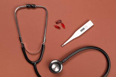 Stethoscope, thermometer and pills on brown background, flat lay. Medical treatment