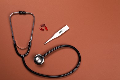 Stethoscope, thermometer and pills on brown background, flat lay. Space for text