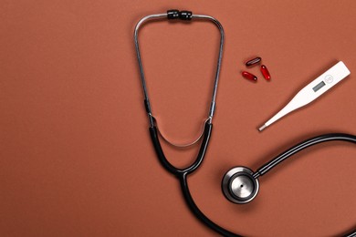 Stethoscope, thermometer and pills on brown background, flat lay. Space for text