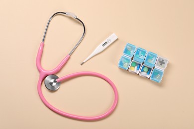 Stethoscope, thermometer and pills on beige background, flat lay. Medical treatment