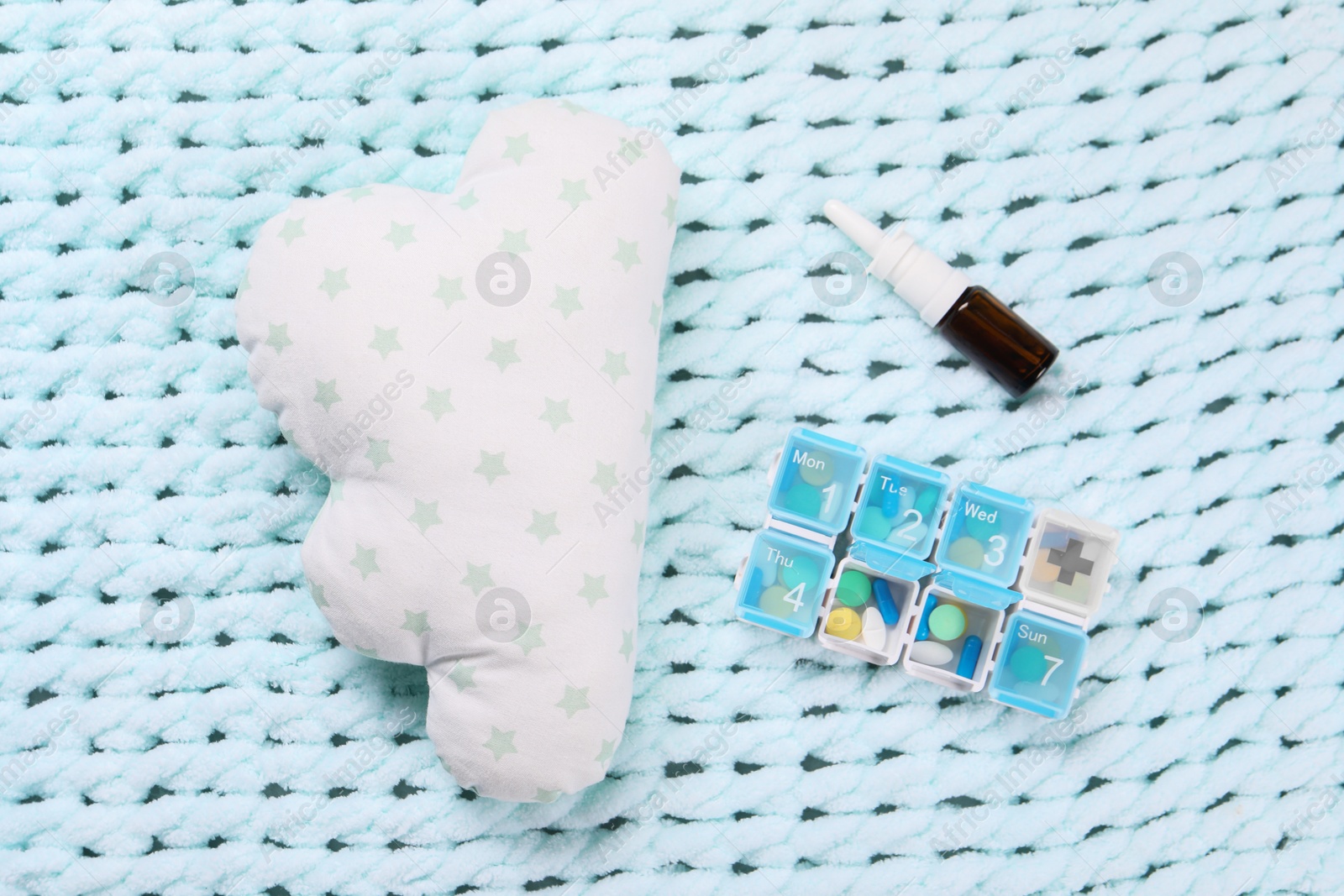 Photo of Pillow, pills and nasal spray on light blue blanket, flat lay