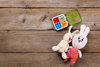 Photo of Toy bunnies and pills on wooden background, flat lay. Space for text