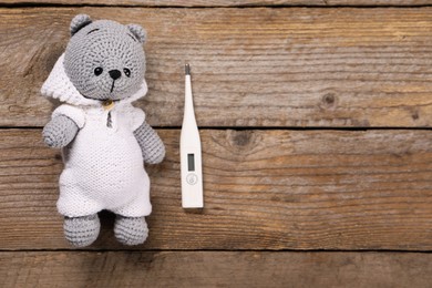 Toy bear and thermometer on wooden background, flat lay. Space for text