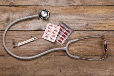 Stethoscope, thermometer and pills on wooden background, flat lay. Medical treatment