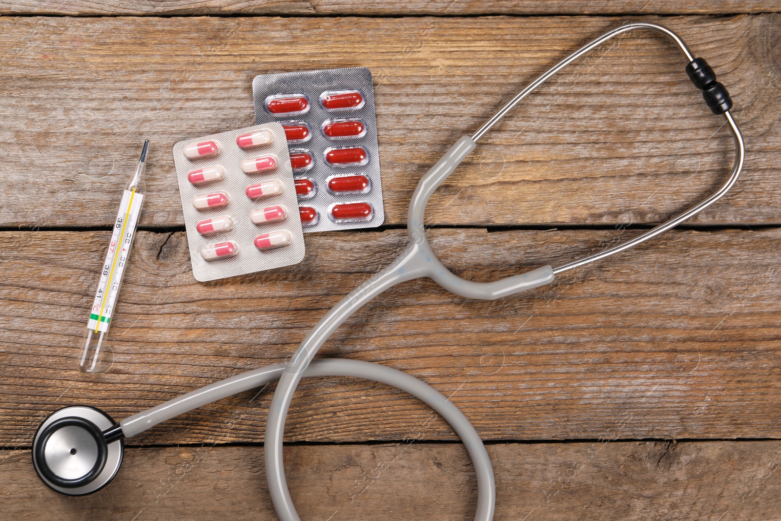 Photo of Stethoscope, thermometer and pills on wooden background, flat lay. Medical treatment