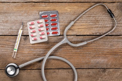 Stethoscope, thermometer and pills on wooden background, flat lay. Medical treatment