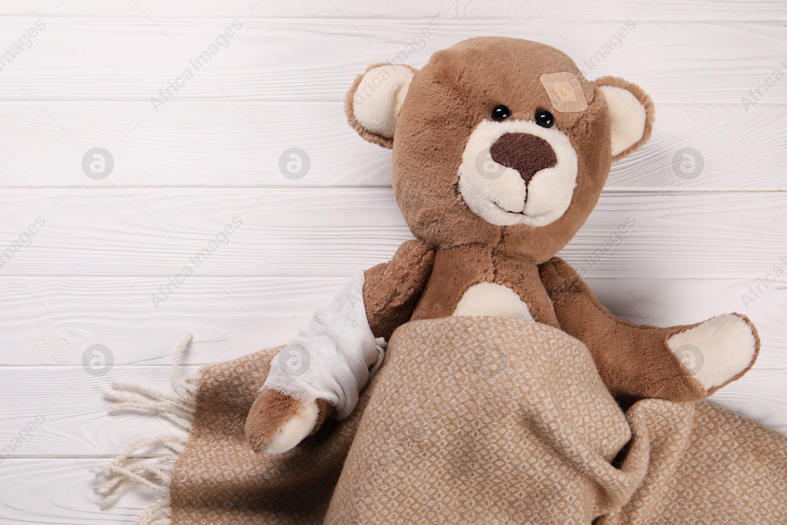 Photo of Toy bear with bandage and medical plaster under blanket on wooden background, top view. Space for text