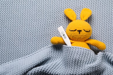 Photo of Toy bunny with thermometer under blanket, top view. Space for text