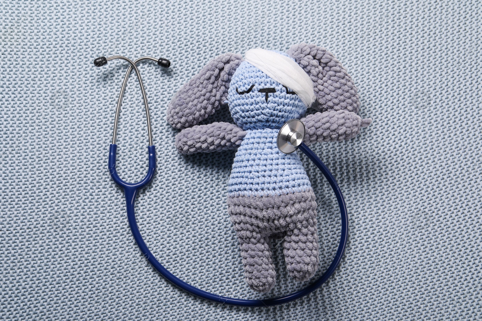 Photo of Toy bunny and stethoscope on gray blanket, top view