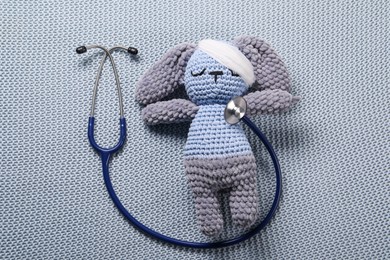 Toy bunny and stethoscope on gray blanket, top view