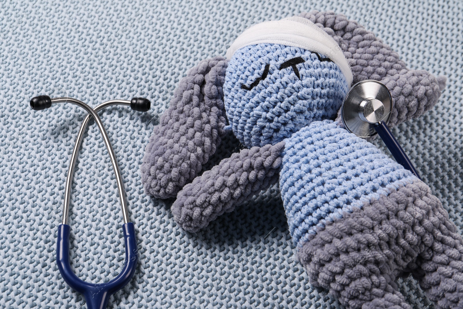 Photo of Toy bunny and stethoscope on gray blanket, closeup