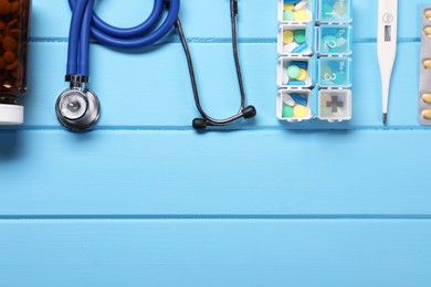 Photo of Stethoscope, thermometer and pills on light blue wooden background, flat lay. Space for text