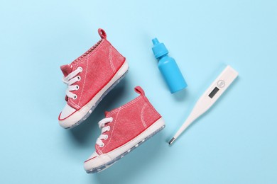 Kid's sneakers, thermometer and nasal spray on light blue background, flat lay