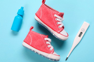 Kid's sneakers, thermometer and nasal spray on light blue background, flat lay