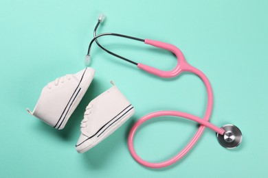 Photo of Stethoscope and kid's sneakers on turquoise background, flat lay