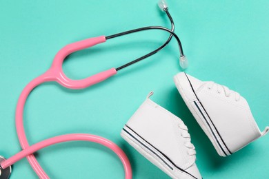 Photo of Stethoscope and kid's sneakers on turquoise background, flat lay