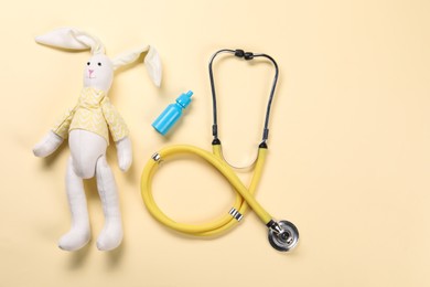 Toy bunny, stethoscope and nasal spray on yellow background, flat lay. Space for text