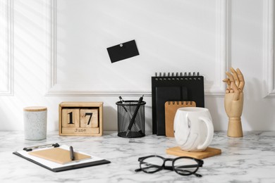 Photo of Stylish office workplace. Decor elements, glasses, cup and stationery on marble table near white wall