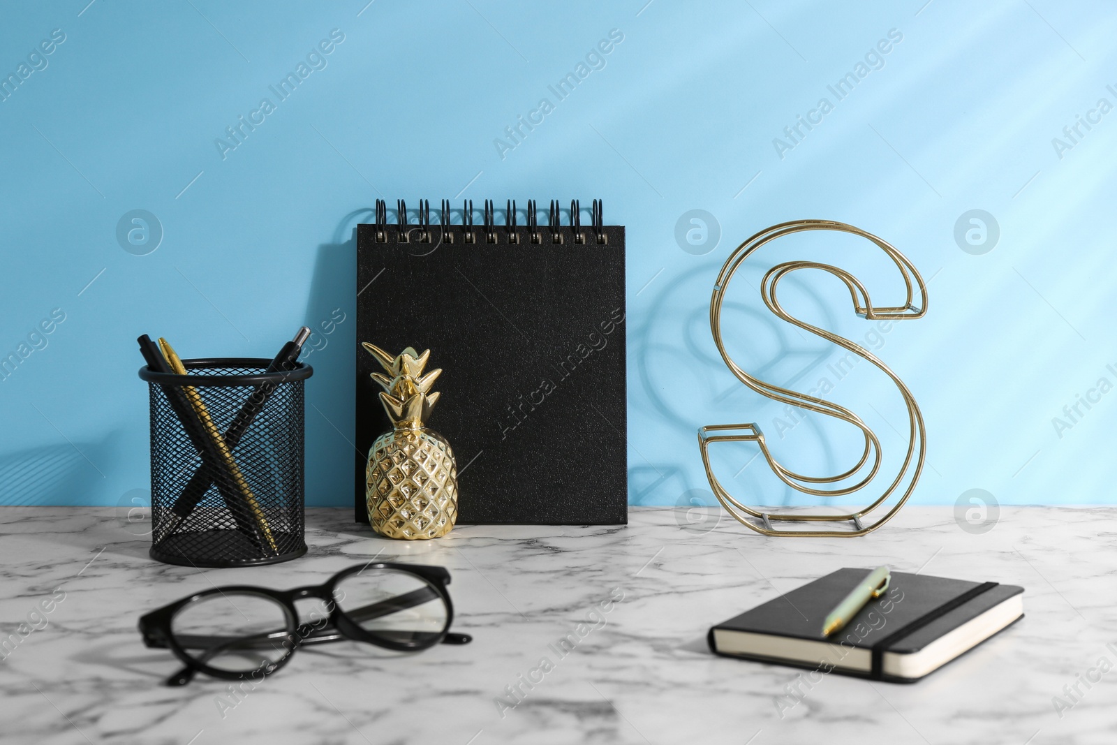 Photo of Stylish office workplace. Decor elements, glasses and stationery on white table near light blue wall